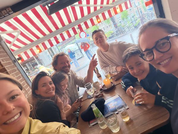 This photo captures a lively group of friends and family gathered inside a cafe, with a distinctive red and white striped awning visible through the window